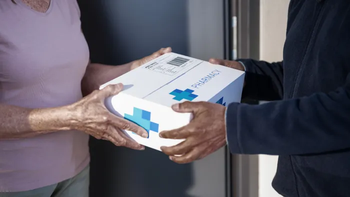 A delivery person handing a pharmacy package to a customer at their door