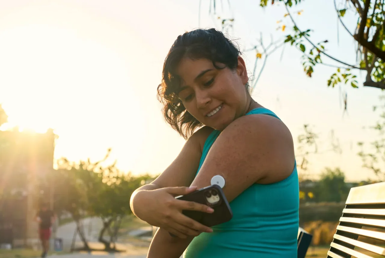 A woman checking her continuous glucose monitor with her phone while outdoors at sunset